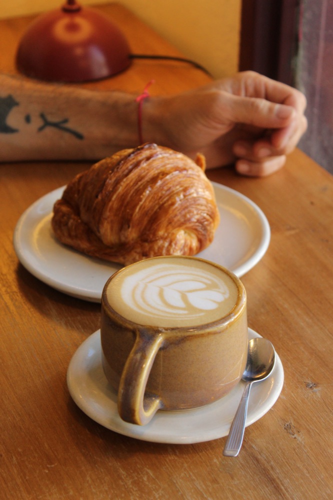 Cappu con latte art y medialuna en mesa de madera